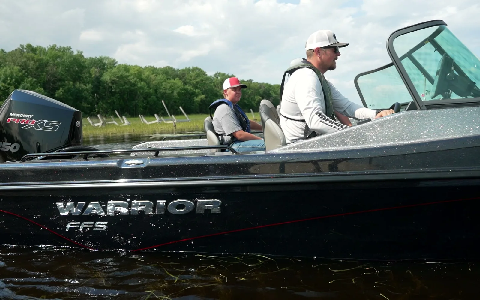 A Warrior FFS runs left to right at speed with two people aboard, WARRIOR FFS lettering on the hull and a Mercury Pro XS on the transom.