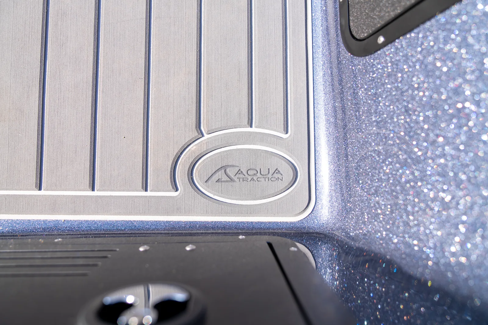 Close-up of a Warrior boat's brushed plank-pattern deck panel with an embossed Aqua Traction logo, next to a sparkling metal-flake surface.