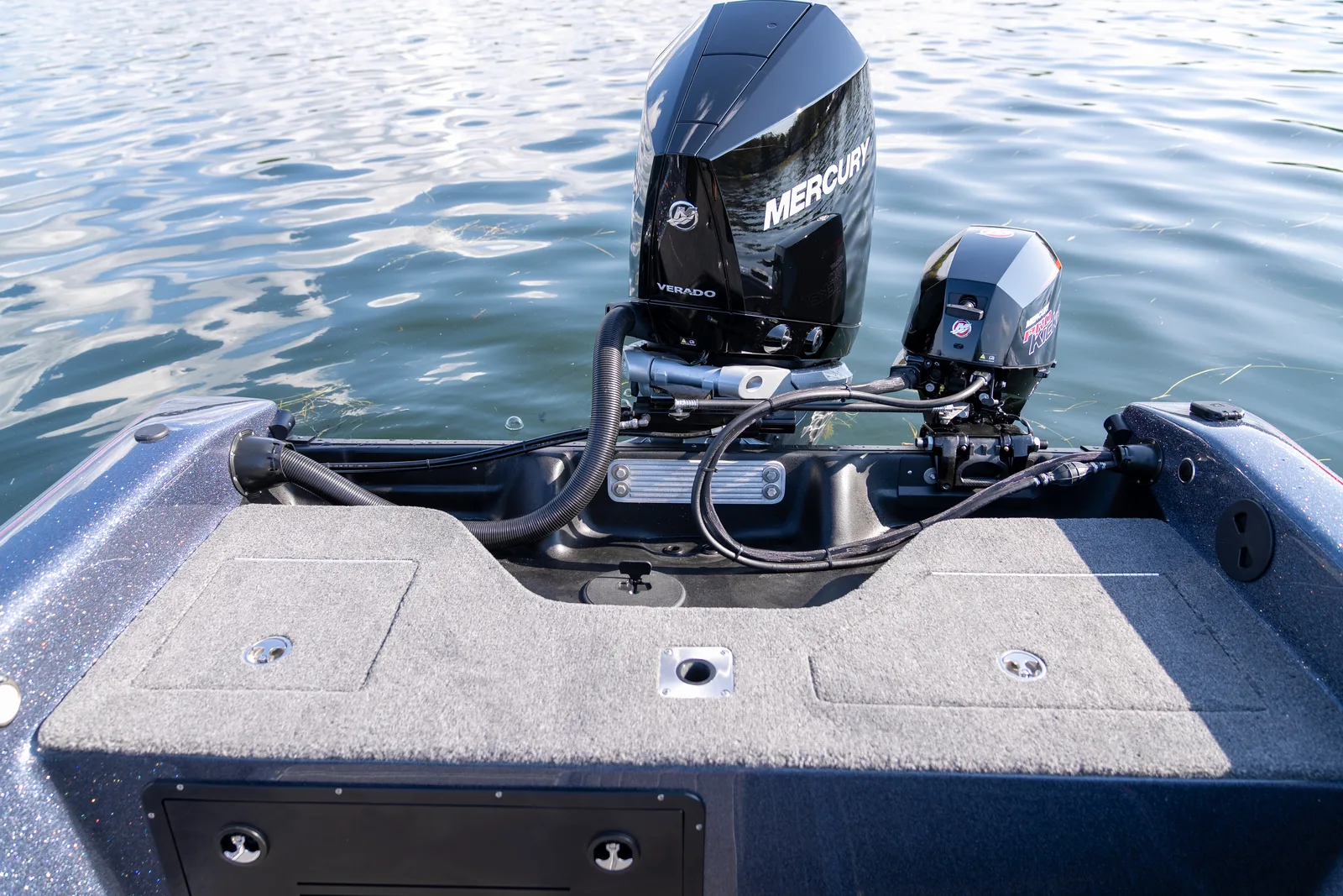Rear deck and transom of the boat with a large Mercury Verado outboard and a smaller kicker motor mounted behind, seen over the carpeted stern deck hatches.