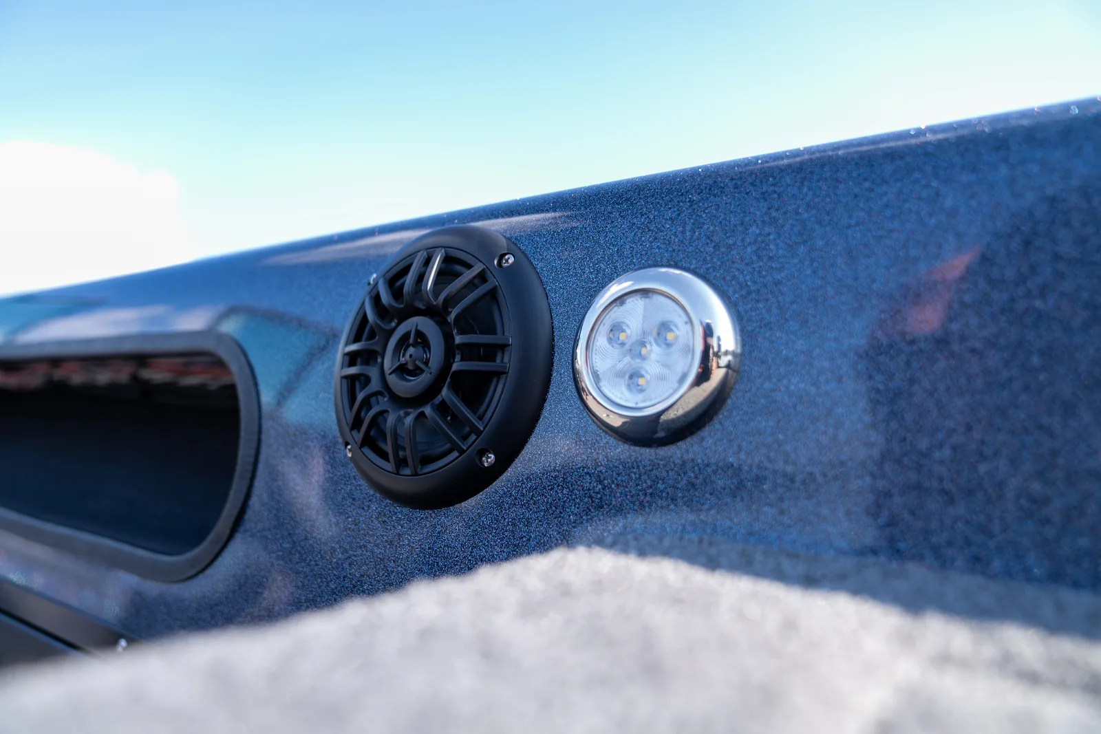 Flush-mounted black speaker and a round chrome LED courtesy light set into the blue metal-flake interior side panel of the boat.