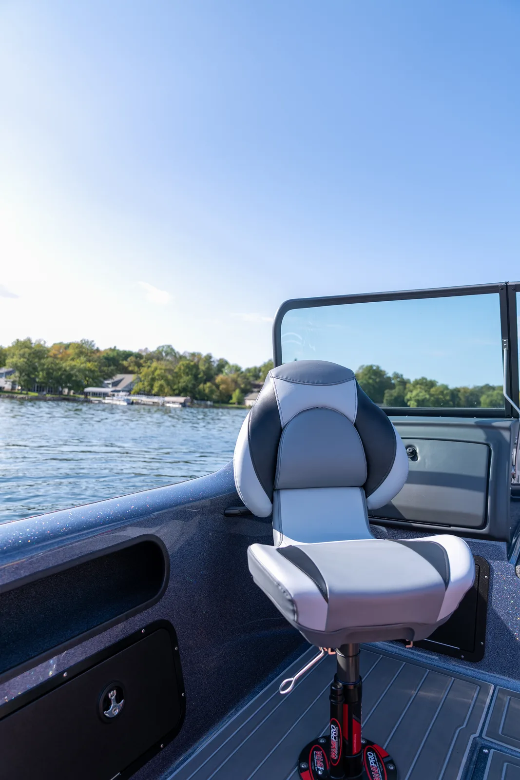 A grey and charcoal bucket seat on a swivel pedestal in the cockpit of a fishing boat, with the windshield and console behind it and open water beyond the gunwale.