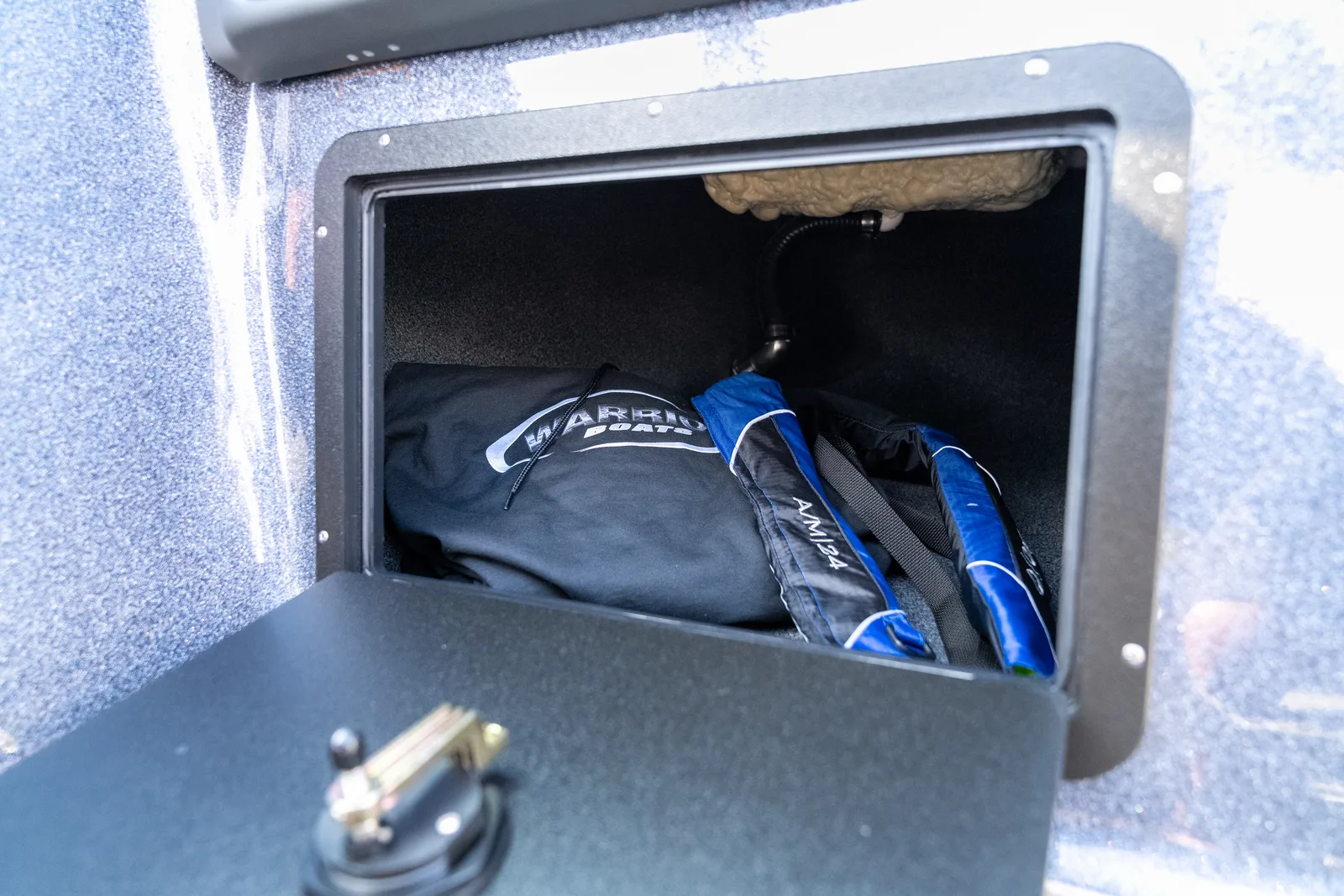 An open storage compartment in a boat's side panel holding a folded black Warrior Boats cover and two blue inflatable life vests.