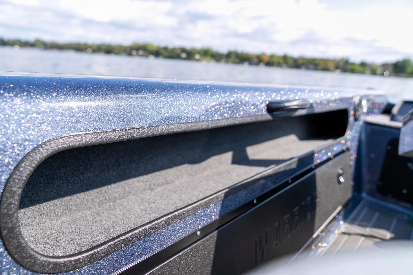 A long open storage channel recessed under the gunwale of a boat, with the lake blurred in the background.