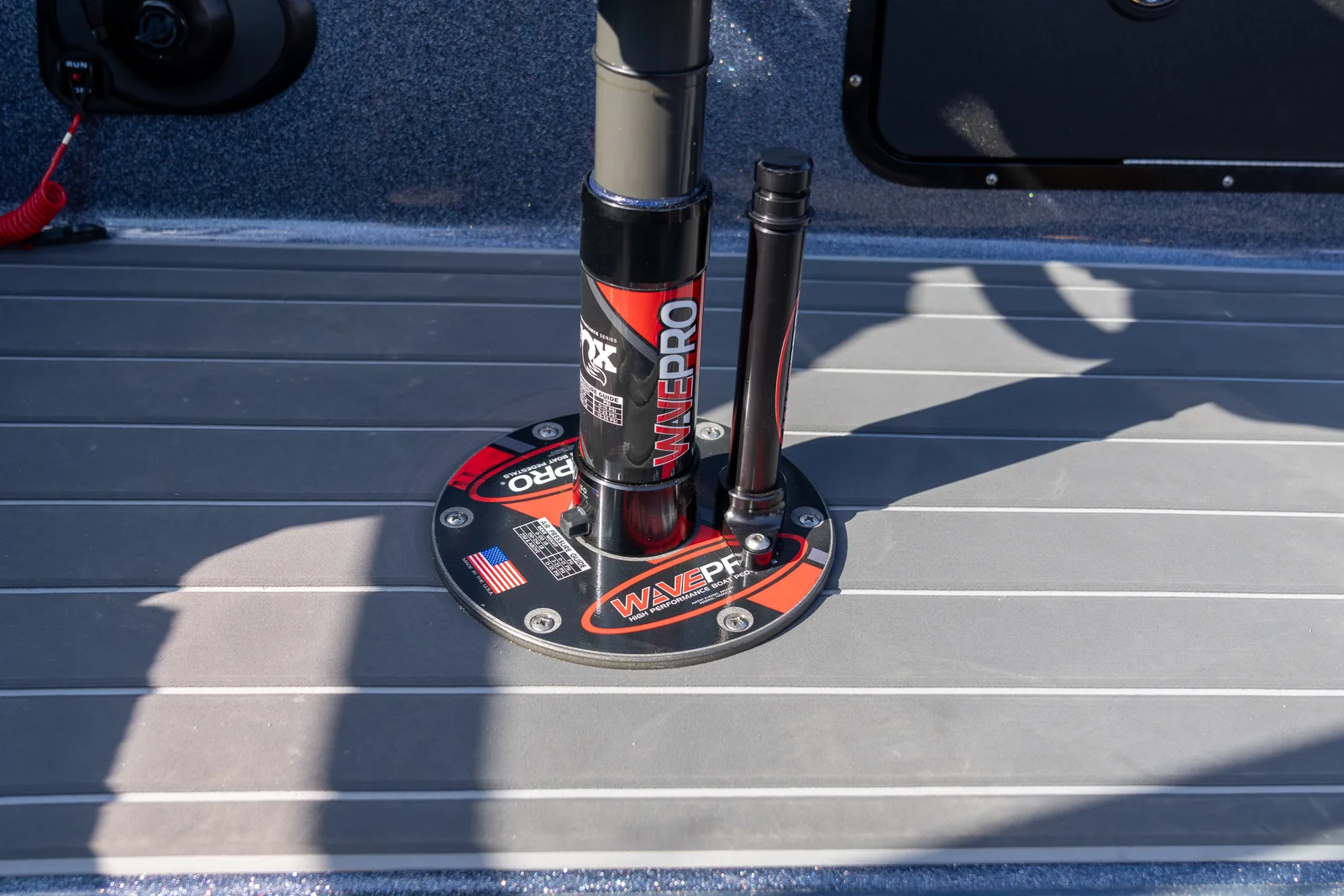 A seat pedestal post rising from a round WavePro base plate bolted to the ribbed cockpit floor of the boat.