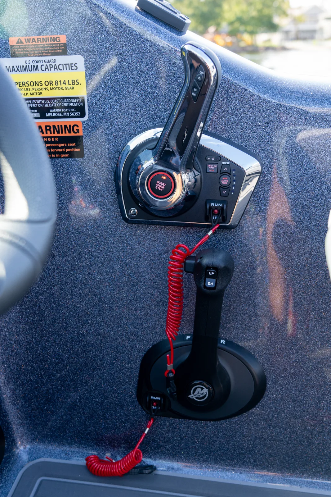 A chrome Mercury throttle and trim control mounted on the boat console above a second black shift lever, both fitted with red coiled lanyard kill switches.