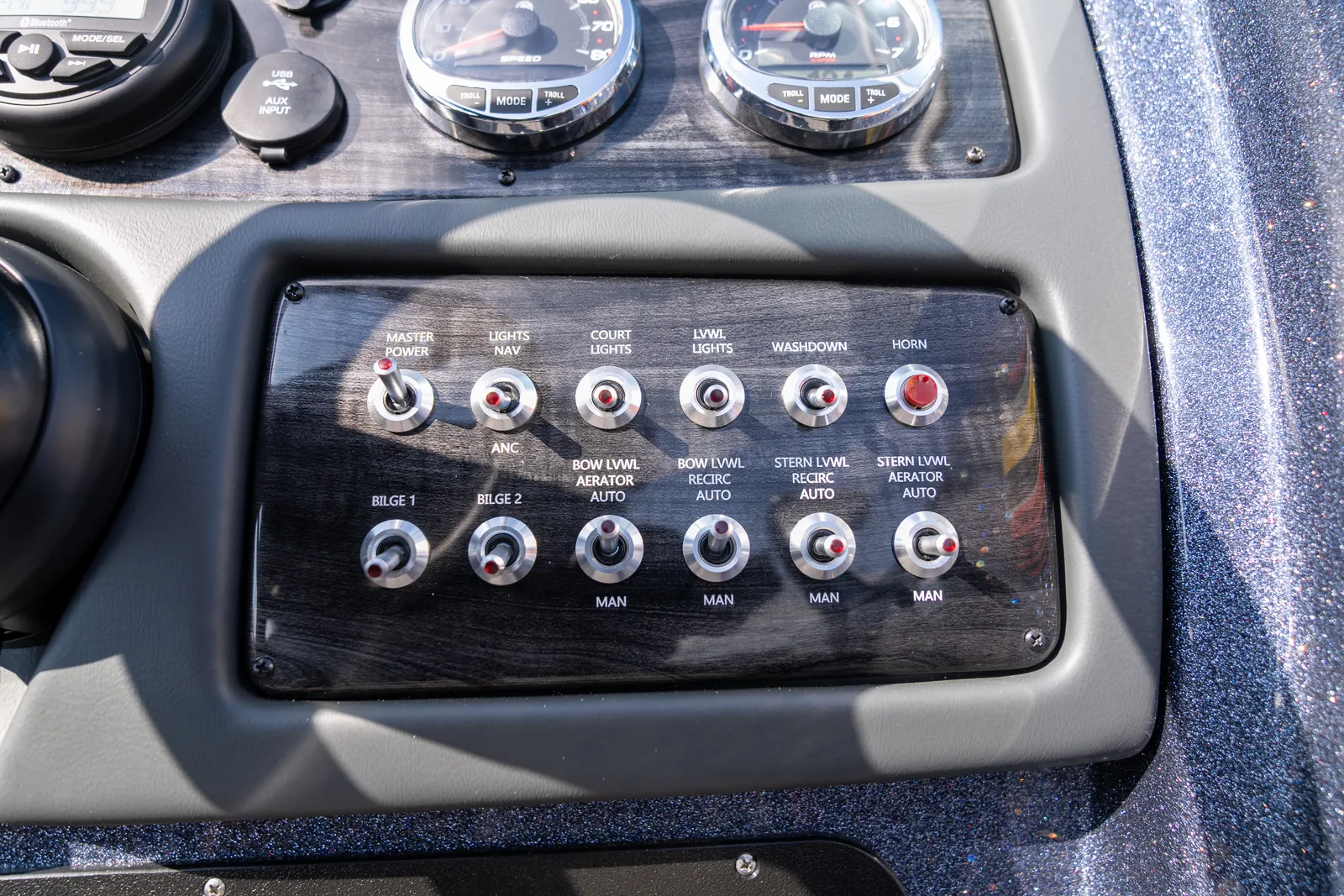 A dark wood-grain switch panel with labelled toggle switches for bilge pumps, livewell aerators and recirculation, navigation and court lights, washdown and horn.