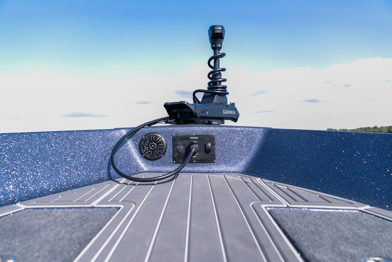 The bow casting deck of a fishing boat with a Garmin trolling motor stowed on the deck, a speaker and an accessory panel with the trolling motor cable plugged in.