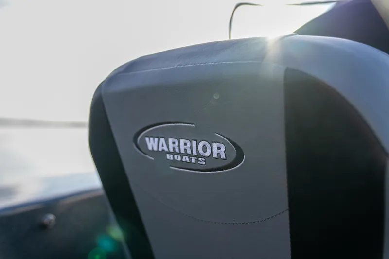 Close-up of a boat seat headrest with an embroidered Warrior Boats logo, backlit by low sun.