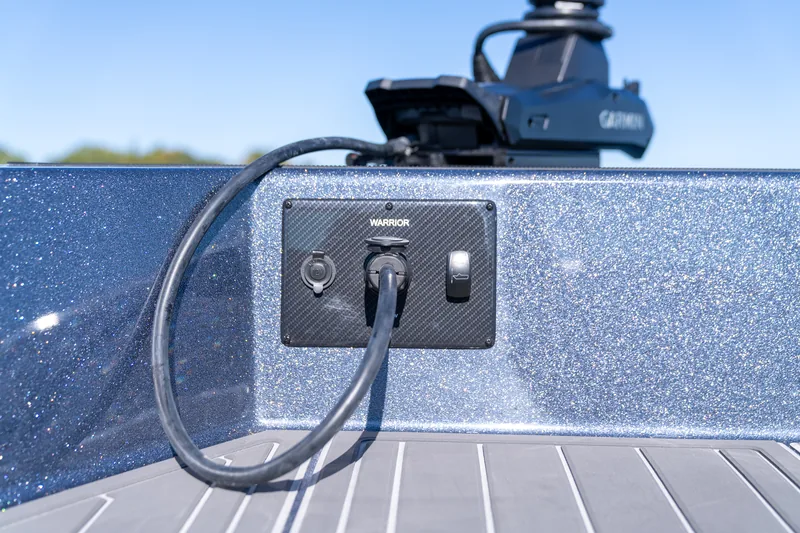 Carbon-look panel on the bow gunwale with a trolling motor plug and cord, accessory outlet and rocker switch, with a mounted electronics unit above.