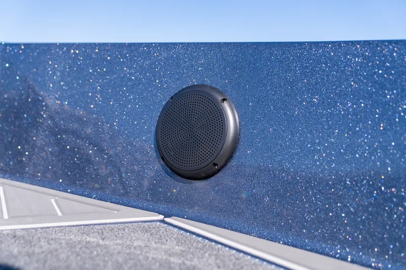 Round black flush-mounted speaker set into the metallic blue bow gunwale under a clear sky.