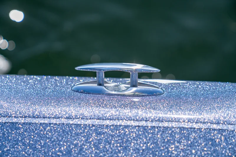 Polished pull-up cleat in the raised position on the sparkling blue gunwale with dark water behind.