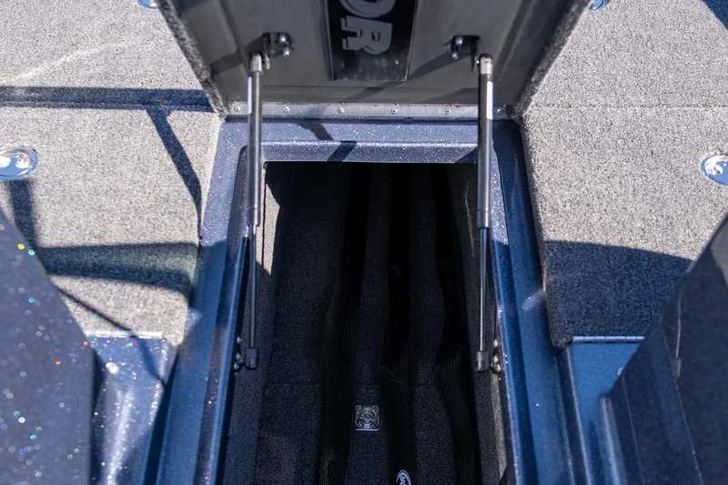 An open center rod locker in the bow deck with gas-strut lids raised and carpeted rod tubes inside.