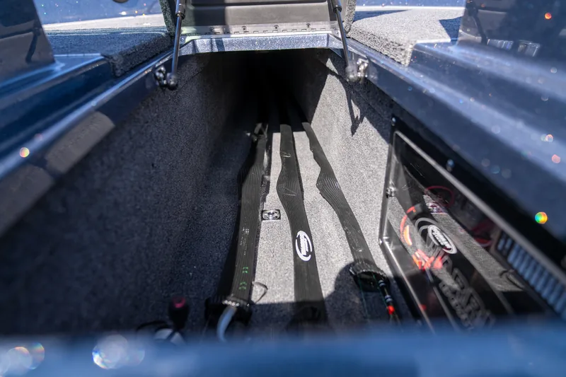 An open side rod locker running along the gunwale with carpeted rod trays and strap tie-downs inside.