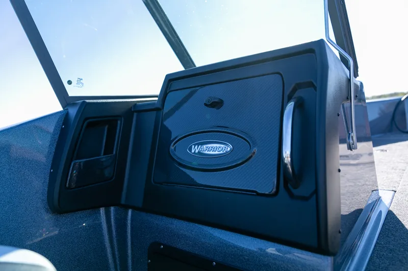 A closed black glove box door on the console with a chrome grab handle and the Warrior oval logo.