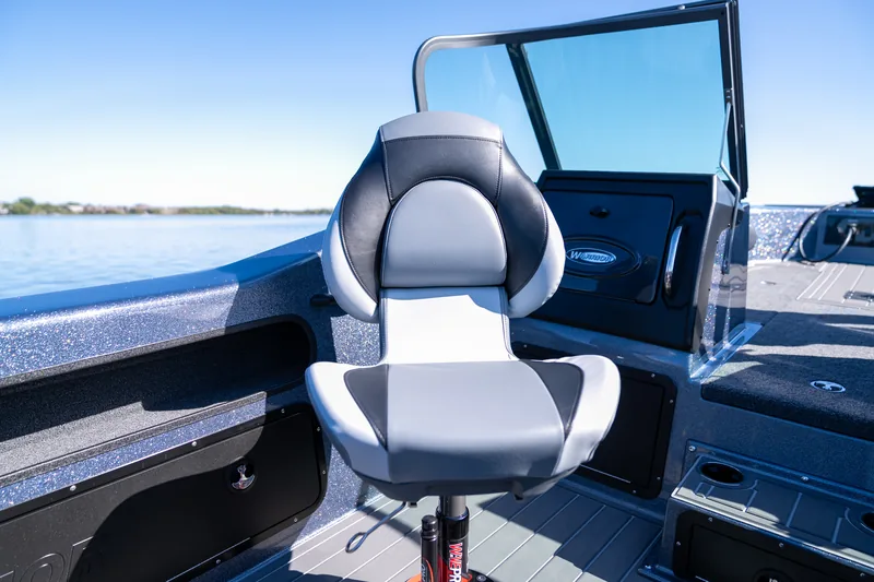 A gray and black upholstered captain's chair at the helm beside the console and windshield with open water behind.