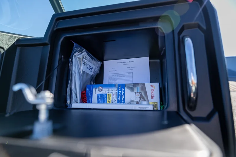 An open glove box compartment holding a dealer pre-delivery checklist, a fire extinguisher box and a sealed plastic pouch.