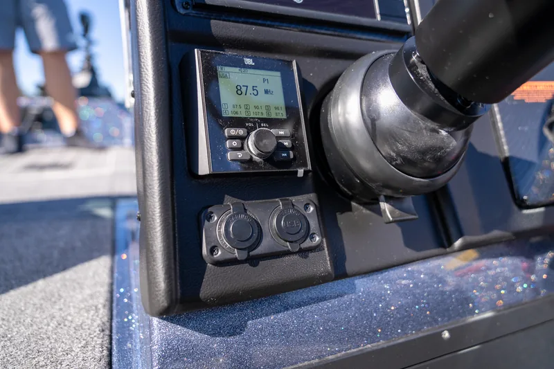 A marine stereo head unit and two round accessory ports mounted on the console beside the throttle.