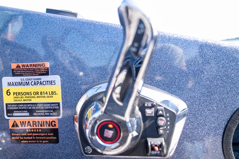 A chrome side-mount throttle and shift control next to Coast Guard capacity and warning decals on the hull side.