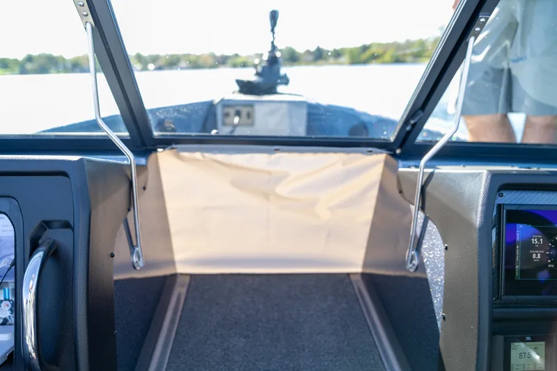View forward through the center walk-through windshield with a canvas closure panel and the lake ahead.