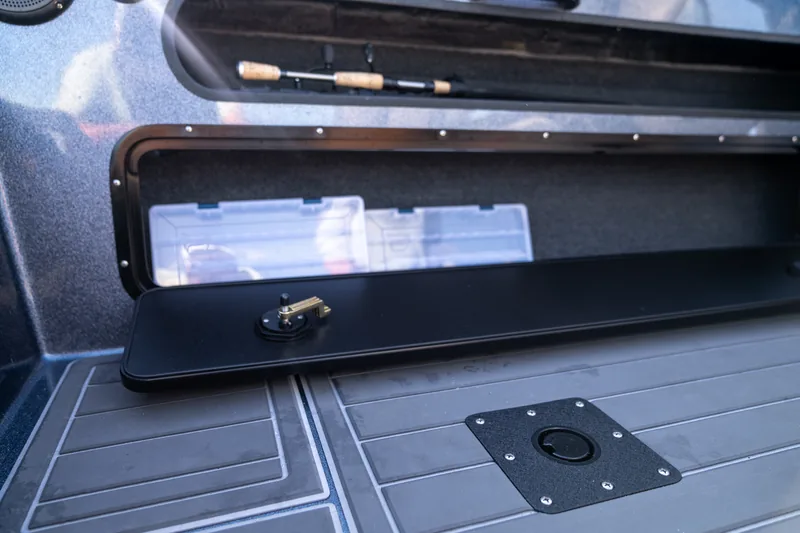 Open tackle storage compartment with clear plastic tackle trays inside, above a gray textured deck.