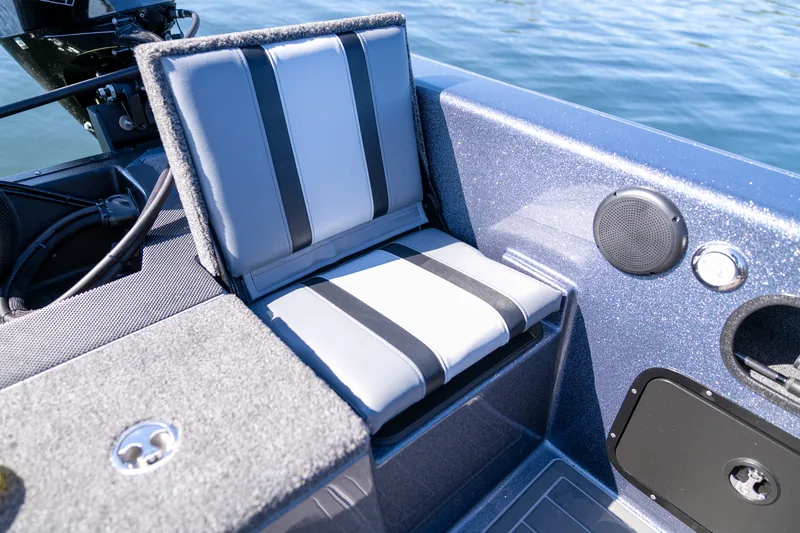 A gray and black upholstered flip up jump seat folded down in the rear cockpit beside a speaker and cup holder.