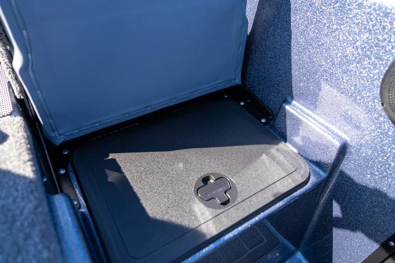 A jump seat cushion tipped up to reveal a latched storage compartment lid underneath.