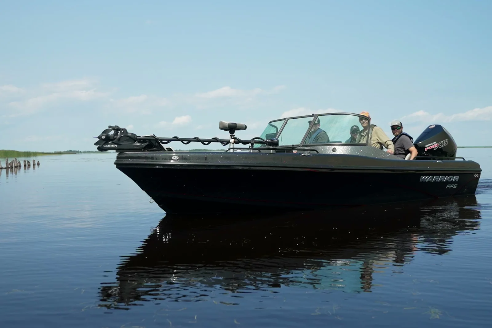 The Warrior FFS at rest on glassy water with two anglers aboard, the trolling motor stowed on the bow and the boat's reflection below.