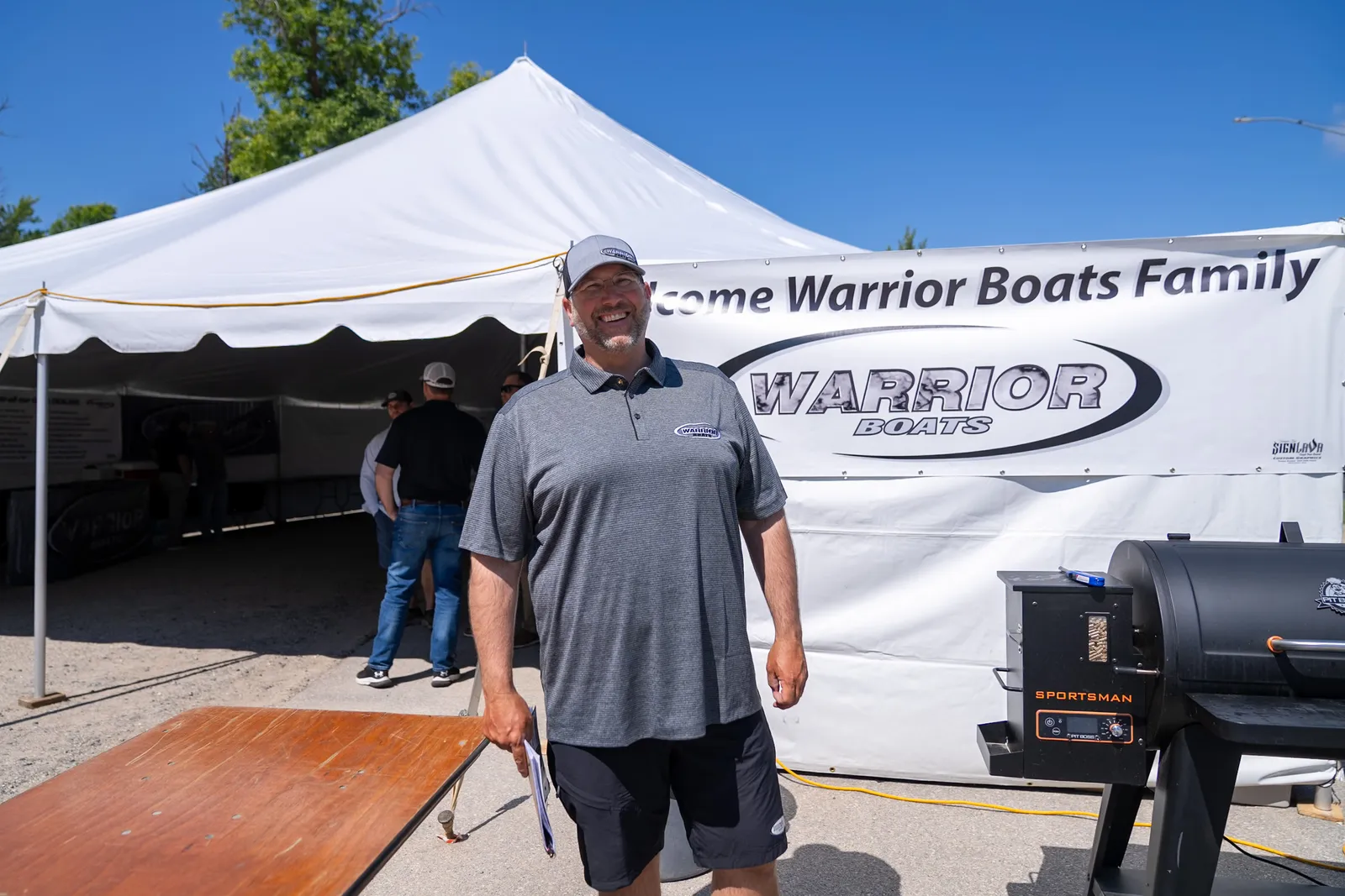 Owners gathered under the white welcome tent at rally check-in, the Warrior Boats Family banner strung across it.