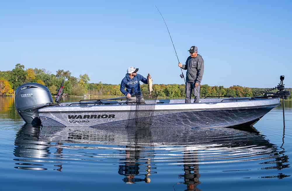 Two anglers landing a fish from a Warrior V2090 against an autumn treeline
